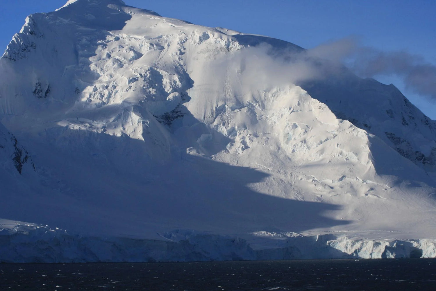 Snow covered mountain peak with wispy clouds.